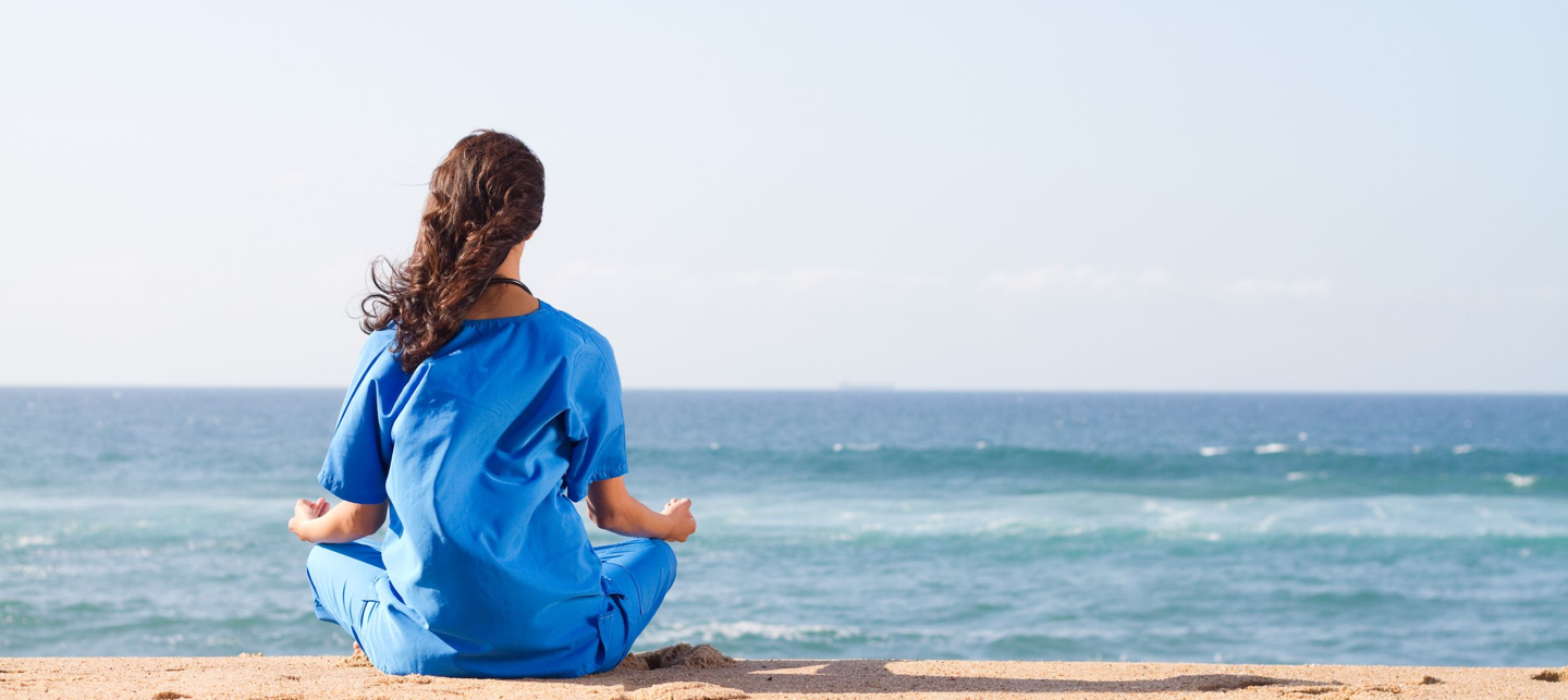 A female nurse sitting on a beach looking at the sea.